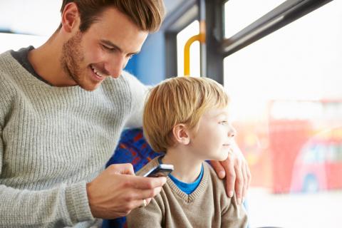 A father looks at his phone while riding the bus with his son.