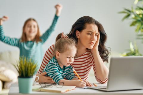 A busy mother looks worried at her computer as her children play around her.