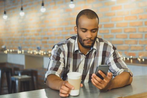 Father stares at a message on his phone while drinking a coffee in a cafe.