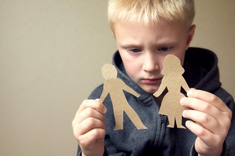 Little boy looks sadly at paper cut-outs of a mom and dad.