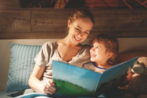 A woman reads a book to her child in bed.