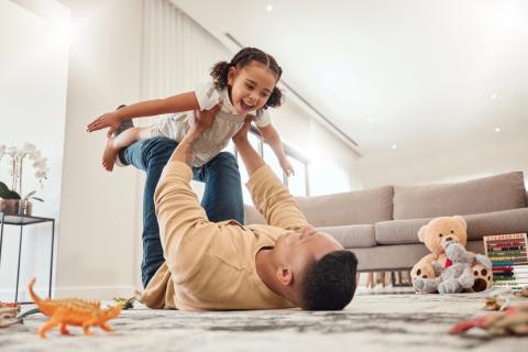 A father lays on the ground as he holds his happy, young daughter in the air