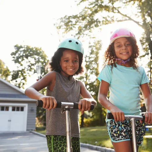 Two young girls playing on scooters in a driveway