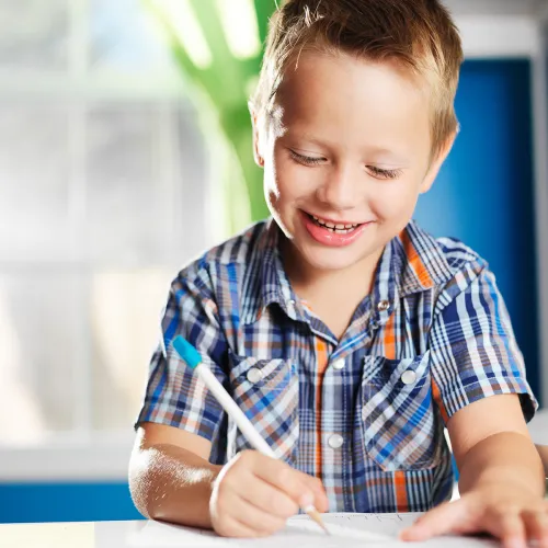 Smiling child sits at desk writing on a piece of paper.