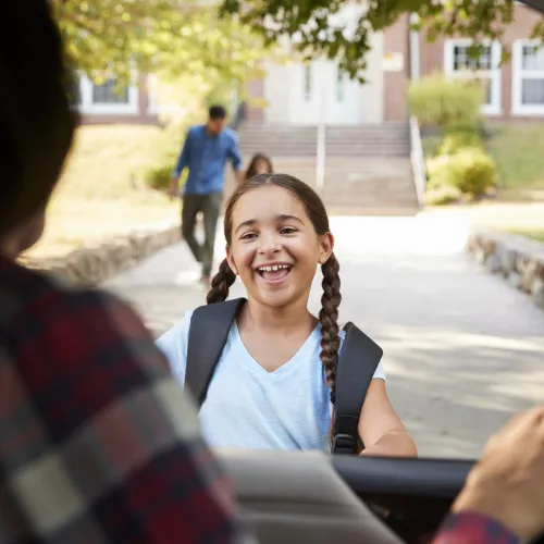Young girl runs up to parent's car with a smile on her face outside of her school.