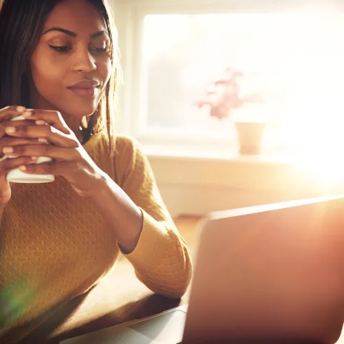 A woman sips coffee while working at her computer.