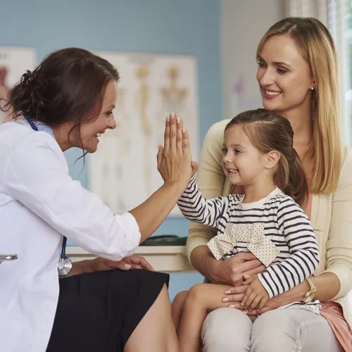 Pediatrician gives little girl sitting on her mother's lap a high five. 