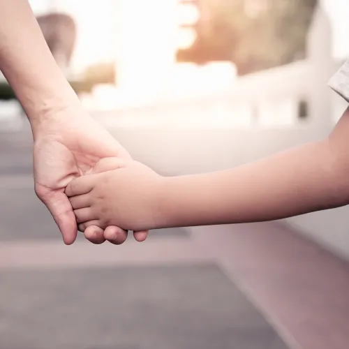 Parent holds the hand of a young child