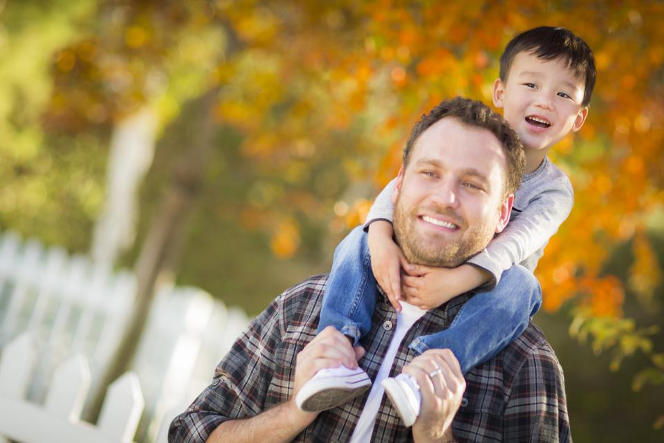 Father gives young son a piggy back outside during the fall.