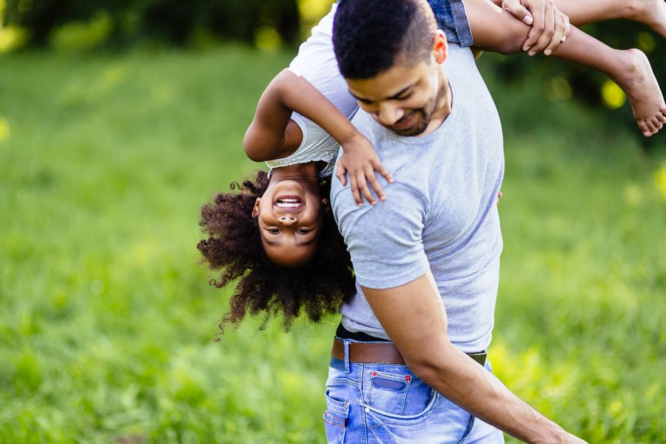 Father carries laughing daughter over his shoulder while playing outside