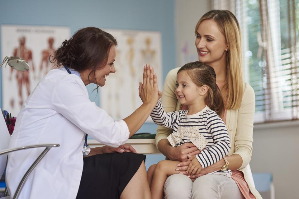 Pediatrician gives little girl sitting on her mother's lap a high five. 